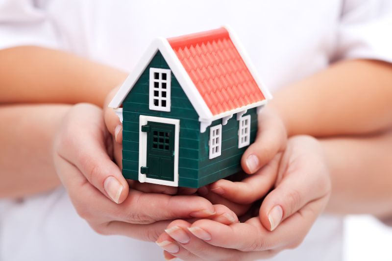 Image shows hands holding a toy house.
